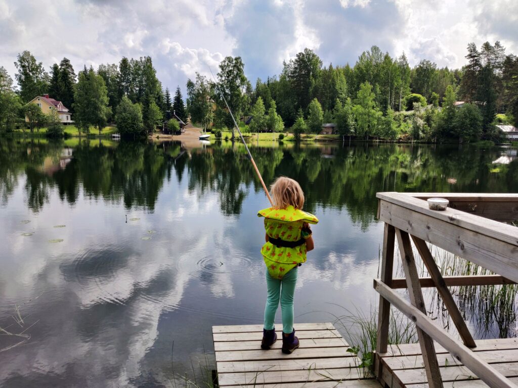 pieni tyttö onkii laiturilla lammesta selkä kameraan päin